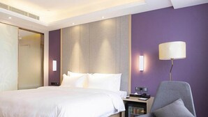 Ein Hotelzimmer mit einem Bett, einem Sessel, einem Schreibtisch mit Lampe und einer Minibar.