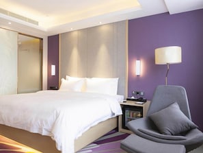 Et hotelværelse med seng, stol, skrivebord med lampe og minibar.