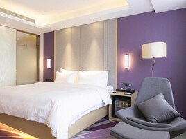 Una habitación de hotel con cama, una silla, un escritorio con lámpara y un minibar.