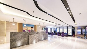 A modern hotel lobby with a marble reception desk, seating area, and large windows. - Lavande Hotels (Weihai)
