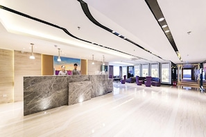 A modern hotel lobby with a marble reception desk, seating area, and large windows. - Lavande Hotels (Weihai)
