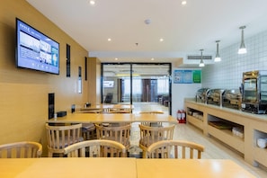 A modern dining area with wooden tables and chairs, a digital menu display, and a kitchen counter with food display. - Lavande Hotels (Weihai)