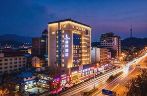 A multi-story hotel with illuminated signage, a prominent entrance, and a view of the surrounding urban area. - Lavande Hotels (Weihai)