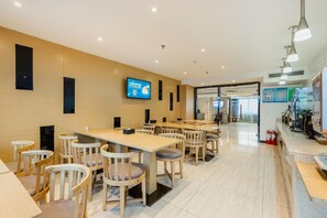 A modern dining area with multiple tables and chairs, a flat-screen TV mounted on the wall, and a clean, tiled floor. - Lavande Hotels (Weihai)