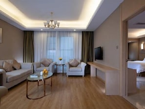 Hotellihuone, jossa on sohvaryhmä, sohvapöytä, televisio ja sänky.