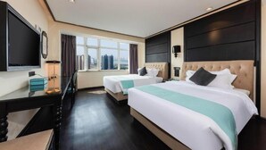 Ein Hotelzimmer mit zwei Betten, einem Fernseher, einem Schreibtisch und einem Fenster mit Blick auf die Stadt.