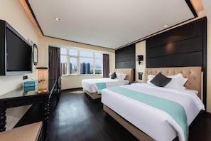 Habitación de hotel con dos camas, televisión, escritorio y ventana con vistas a la ciudad.