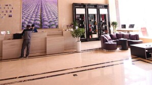 Eine Hotelhalle mit einer Rezeption, einem großen Gemälde einer Lavendelfeldlandschaft, einer Sitzecke mit Sofas und einem Bücherregal.
