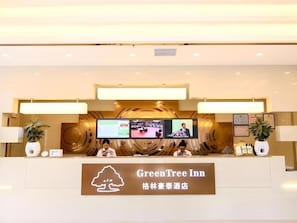 Ein Empfangstresen mit einem Schild, auf dem 'GreenTree Inn' steht, und mehreren Monitoren darüber.
