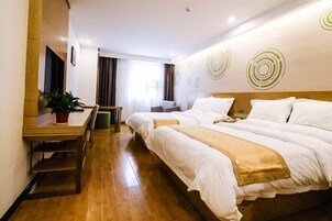 Habitación de hotel con dos camas, un escritorio, una silla, una planta en maceta y una ventana con cortinas.