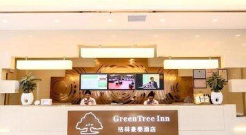 Una recepción en GreenTree Inn con una pantalla digital, dos recepcionistas y un letrero con el nombre del hotel.