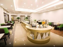 Un comedor moderno con varias mesas y sillas, una estación de buffet central, y un ambiente limpio y bien iluminado.