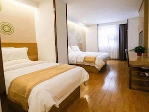 Ein Hotelzimmer mit zwei Betten, Holzboden, einem kleinen Tisch und einem Fenster mit Vorhängen.