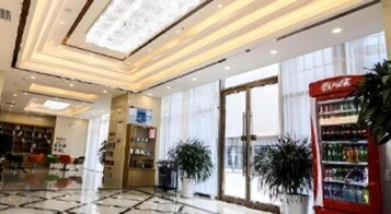 Un hall de hotel con entrada por puerta de cristal, una máquina expendedora y plantas en macetas.