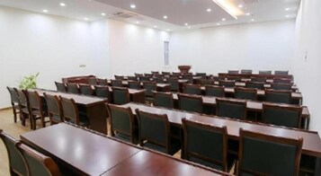 Un salón de conferencias con filas de mesas y sillas, una pizarra y un ventanal.