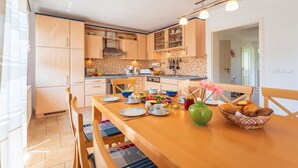 Une cuisine moderne avec des meubles en bois, une table à manger dressée pour deux personnes et un vase rempli de fleurs.