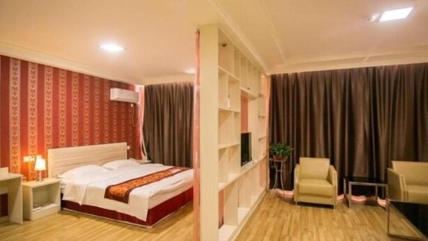 Une chambre d’hôtel comprenant un lit, un coin salon avec des fauteuils, une télévision et une bibliothèque.