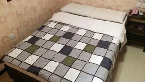 Een bed met een geruit sprei, een nachtkastje met een lamp en een muur met een rond patroon.