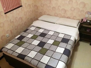 Ein Bett mit karierter Bettdecke, ein Nachttisch mit Lampe und eine Wand mit einem kreisförmigen Muster.