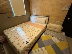 Ein Einzelbett mit floralem Überwurf, ein Nachttisch mit Kissen und eine Wand mit einem kreisförmigen Muster.