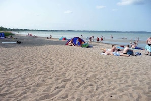 Ein Strand mit badenden Menschen, Zelten und ruhiger See.