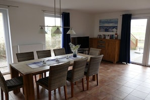 Ein Essbereich mit einem Holztisch, Korbstühlen, einem Fernseher und Blick durch eine Glastür.