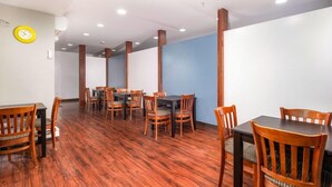 A dining area with wooden tables and chairs, a clock on the wall, and a blue accent wall. - Casco Bay Inn (Freeport)