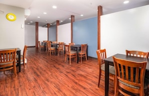 A dining area with wooden tables and chairs, a clock on the wall, and a blue accent wall. - Casco Bay Inn (Freeport)