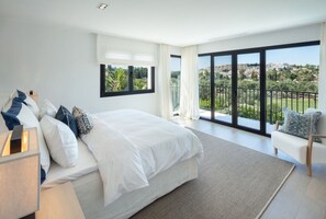 Ein modernes Schlafzimmer mit einem großen Bett, Blick auf eine grüne Landschaft und einem Balkon mit Geländer.