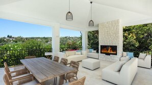 An outdoor living area with a stone fireplace, wicker furniture, and a view of the surrounding landscape. - Vrbo Property (Marbella)
