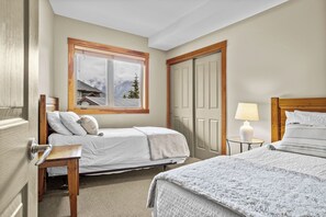 Ett hotellrum med två sängar, ett fönster med utsikt över bergen, en dörr och ett litet bord med en lampa.