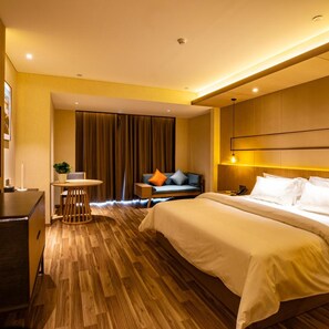 Ein Hotelzimmer mit einem großen Bett, einem Schreibtisch, einem Sessel, einem kleinen Tisch mit Pflanze und einer Couch mit Kissen.