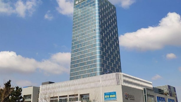 Ein modernes Hochhaus mit Glasfassade, umgeben von einem Gebäude mit flachem Dach und Beschilderung.