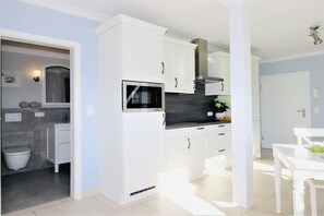 A modern kitchen with white cabinetry, a black countertop, and a built-in microwave. - Holiday apartment with 2 bedrooms (Zingst)