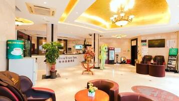 A hotel lobby with a reception desk, seating area, and a large chandelier.
