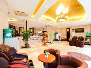 A hotel lobby with a reception desk, seating area, and a large chandelier.