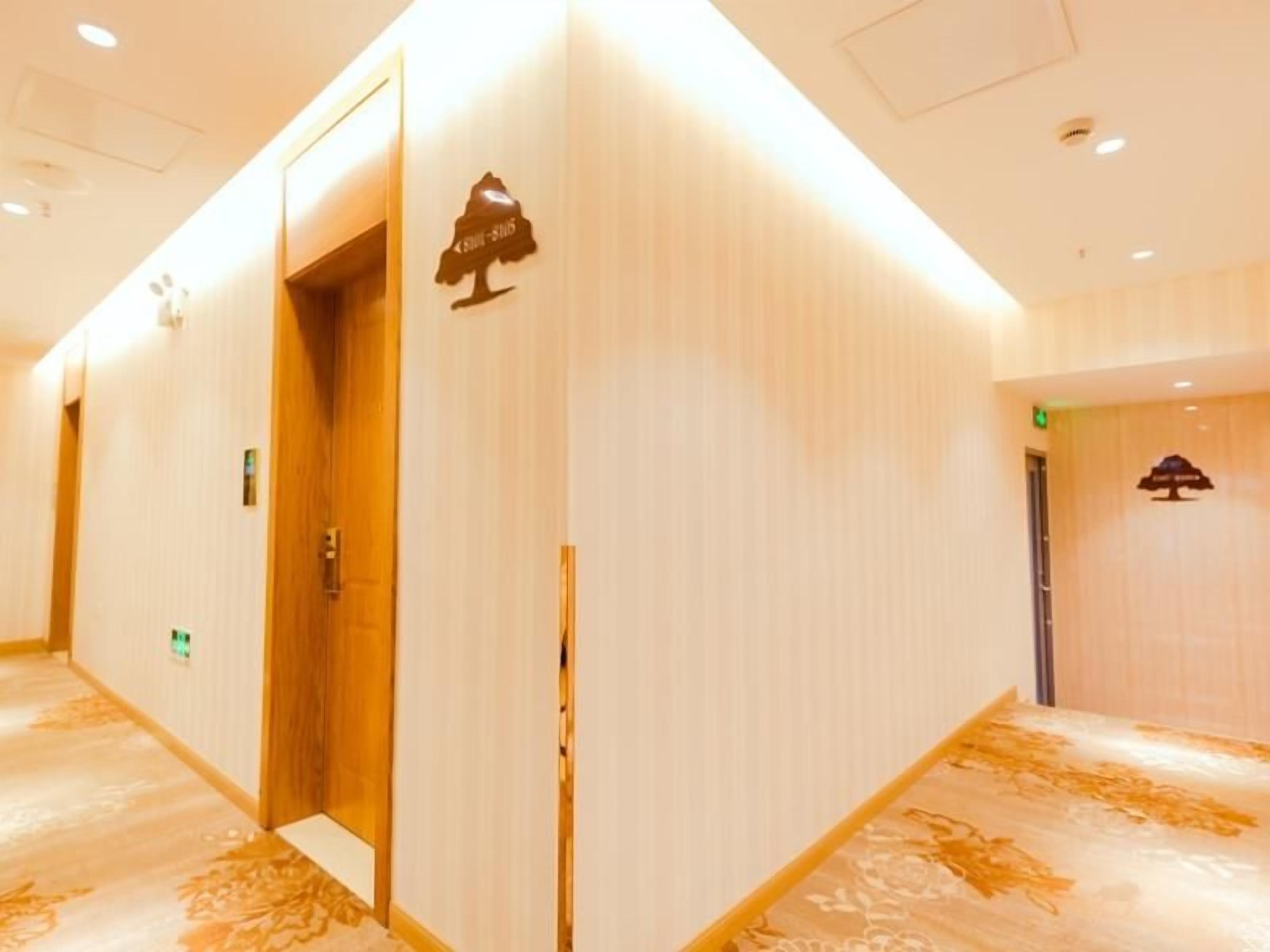 A hotel corridor with wooden doors, a reception area, and a sign indicating a room number.