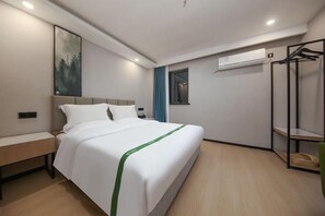 Habitación de hotel moderna con una cama grande, un banco, aire acondicionado de pared y un perchero.