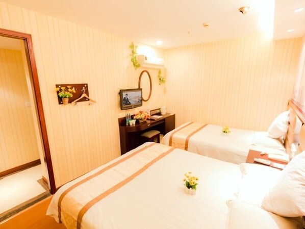 A hotel room with two beds, a desk with a computer, a mirror, and a small plant.