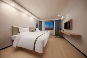 Ein modernes Hotelzimmer mit einem großen Bett, einem Schreibtisch, einem Sessel, einem Fernseher und einem Fenster mit Vorhängen.