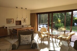 Ein Wohnzimmer mit einer Couch, einem Esstisch, Stühlen und einer Glastür, die in einen Garten führt.