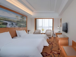 Habitación de hotel con dos camas, un escritorio, una silla, un televisor y un ventanal grande.