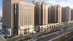 A multi-story hotel with a prominent sign, a parking lot, and a road in the foreground. - Vienna International Hotel (Langfang)