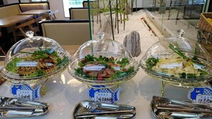 A buffet setup with three covered dishes, each labeled with a blue fish-shaped sign, and a pair of tongs in front of each dish. - Vienna International Hotel (Langfang)