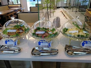 En buffetopstilling med tre overdækkede fade, hver mærket med et blåt skilt i fiskefacon, og en parisergreb foran hver fade.