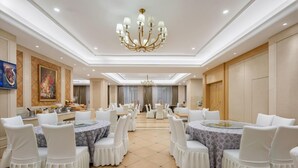 A spacious banquet hall with round tables, white chairs, and a central chandelier. - Vienna International Hotel (Huanggang)