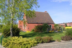 Ein rotes Ziegelhaus mit geneigtem Dach, umgeben von einem gepflegten Garten mit verschiedenen Sträuchern und Blumen.