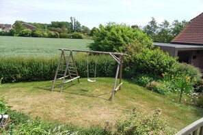 A wooden swing set in a grassy yard with a house and a field in the background. - Holiday home in Fehmarn with 3 bedrooms (Meeschendorf\/ Fehmarn)