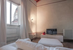 A hotel room with a bed, a TV on a white cabinet, a window with curtains, and a radiator. - Ricasoli Terrace (Florence)
