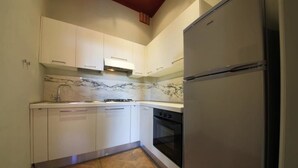 A compact kitchen with white cabinets, a marble backsplash, a stainless steel refrigerator, and a built-in oven.